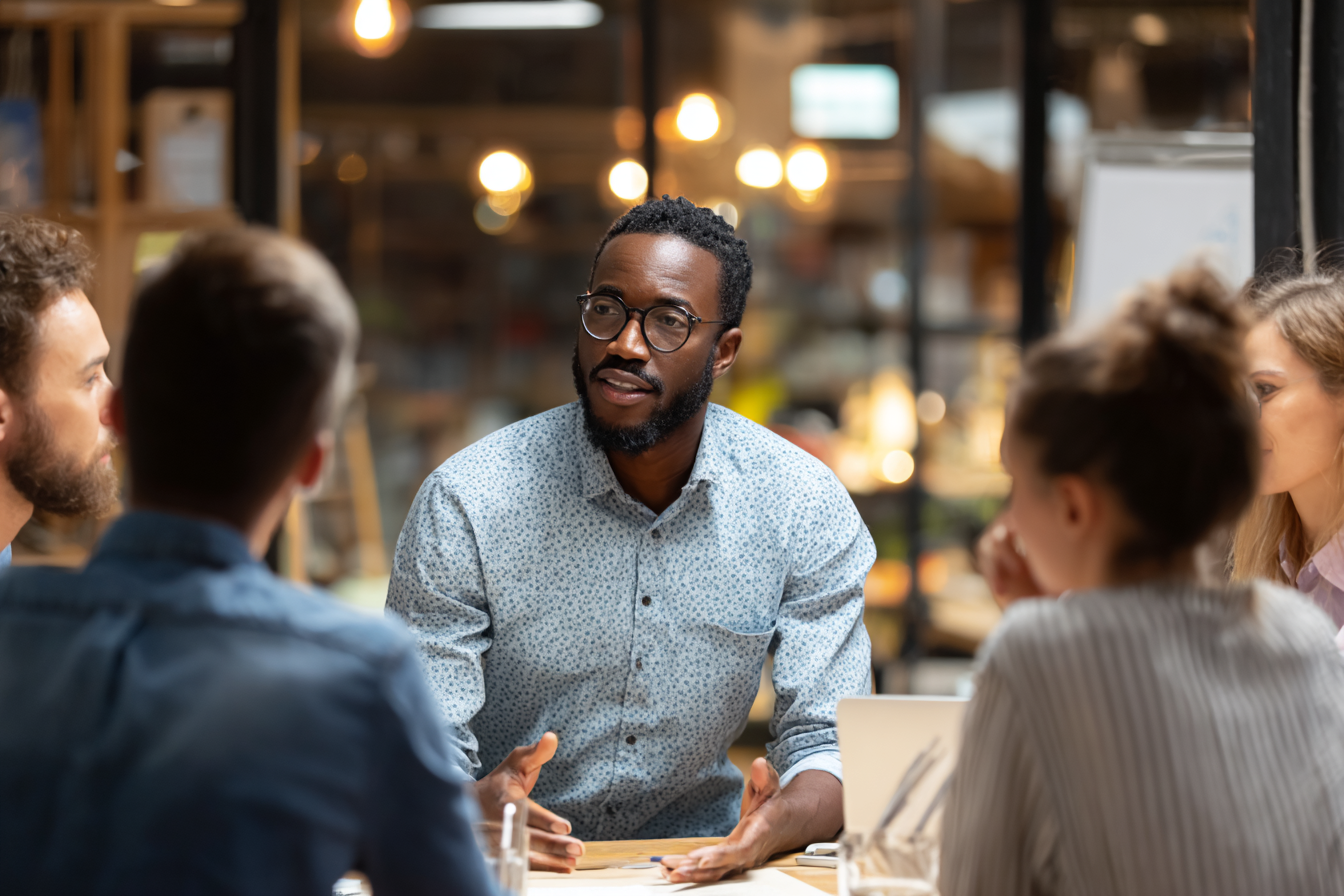Un professionnel anime une discussion d’équipe dans un espace de travail collaboratif, posture ouverte et échanges naturels.